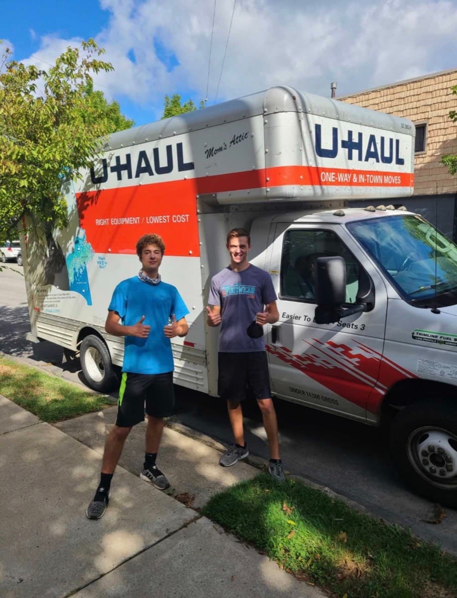 Two DAW movers giving a thumbs up in front of a moving truck on a residential street.