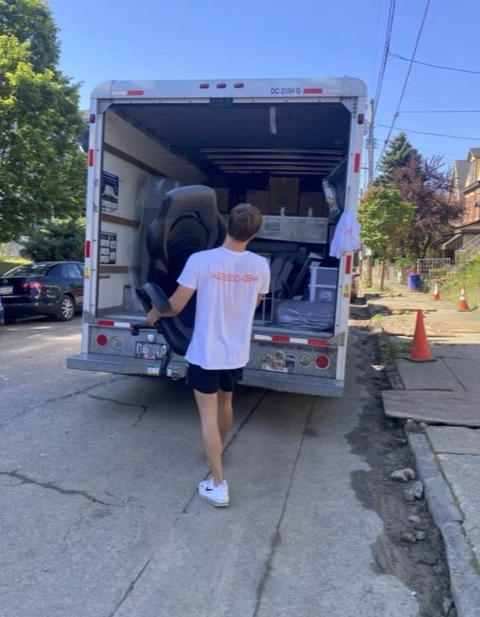 A DAW crew member carrying an office chair to a loaded box truck on a Pittsburgh street.
